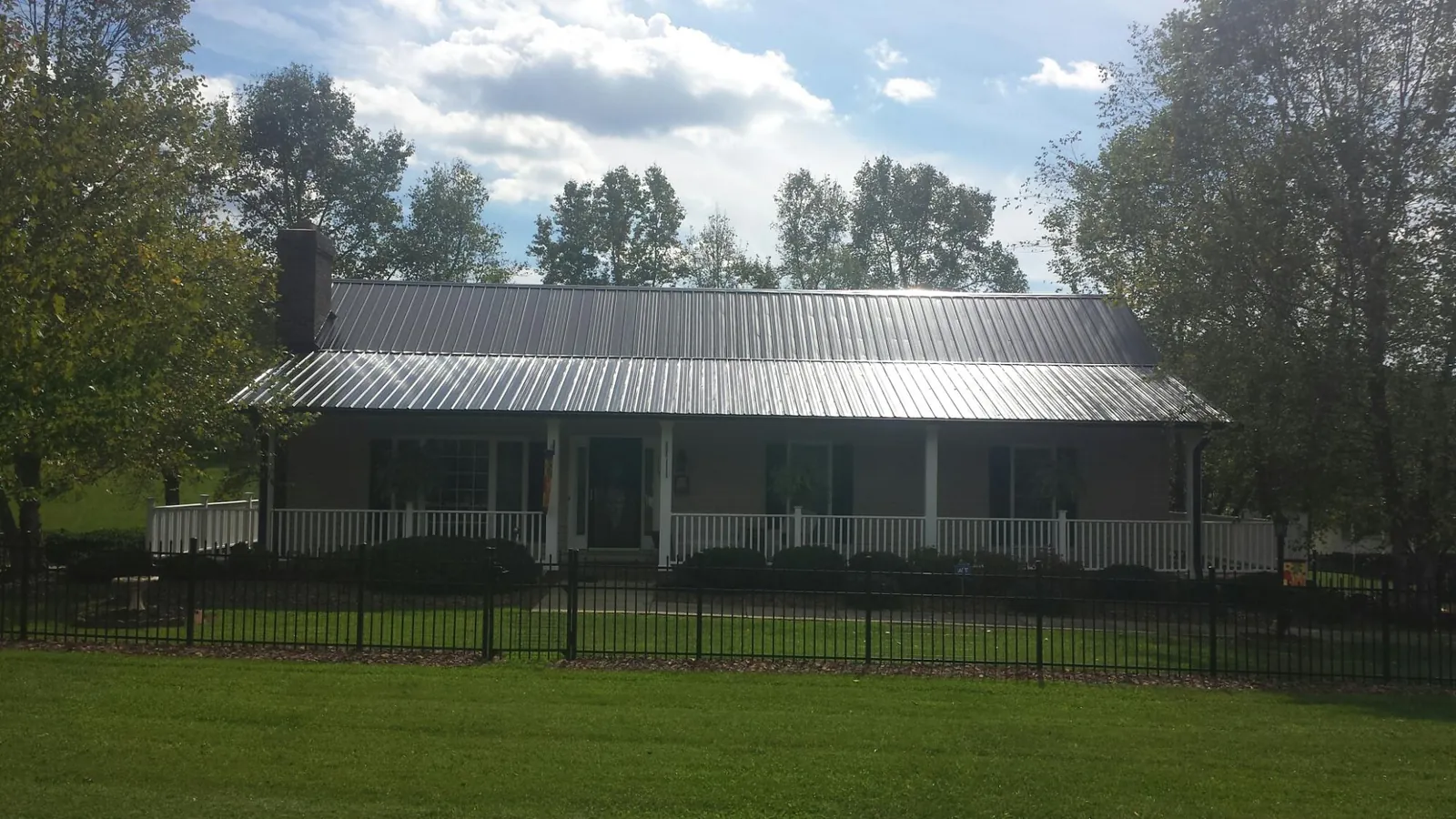 Gray metal roof on a brick ranch with a full width front porch — Gutter Guard Installation work by our crew in Amsterdam