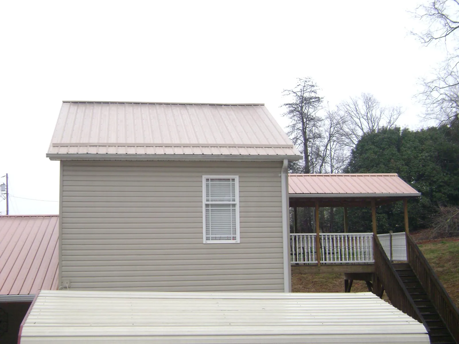 Tan metal roofs on a two story addition and attached porch, from a Roof Replacement job in Amsterdam